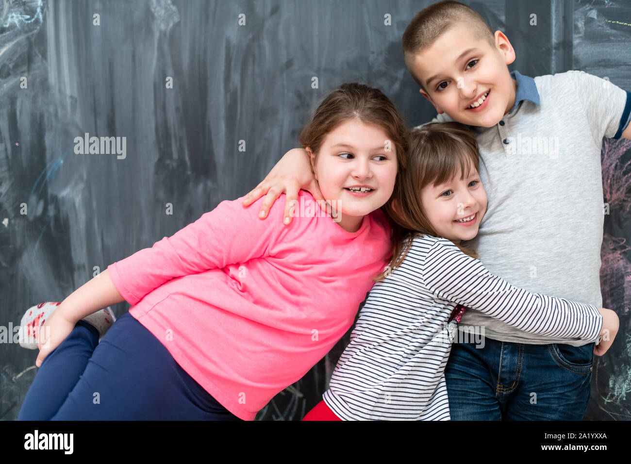 group portrait of happy kids hugging each other while having fun in front of black chalkboard Stock Photo