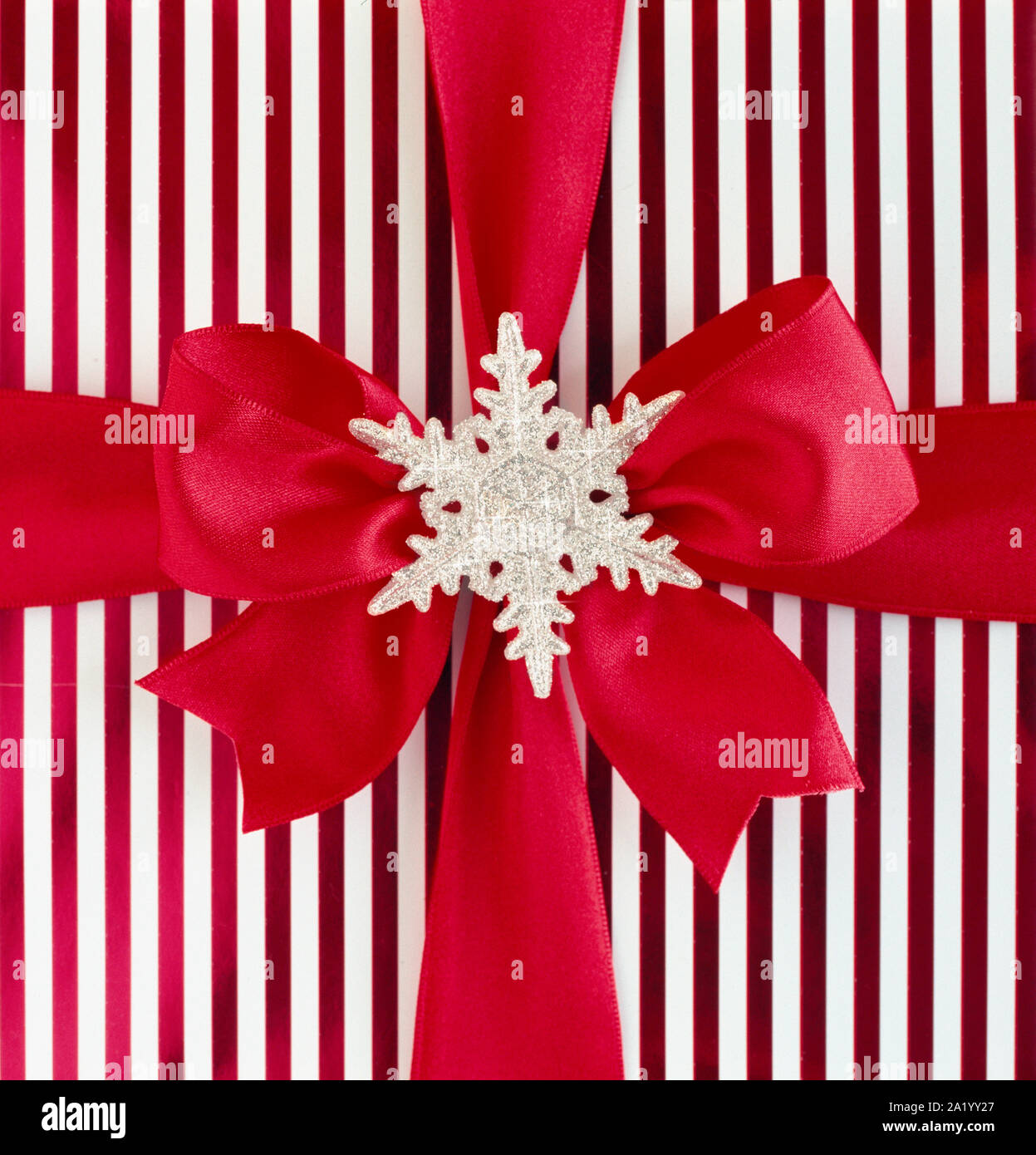 Close-up closeup of red and white striped Christmas gift present with red satin ribbon bow and silver glitter snowflake decoration. Special, fancy hol Stock Photo