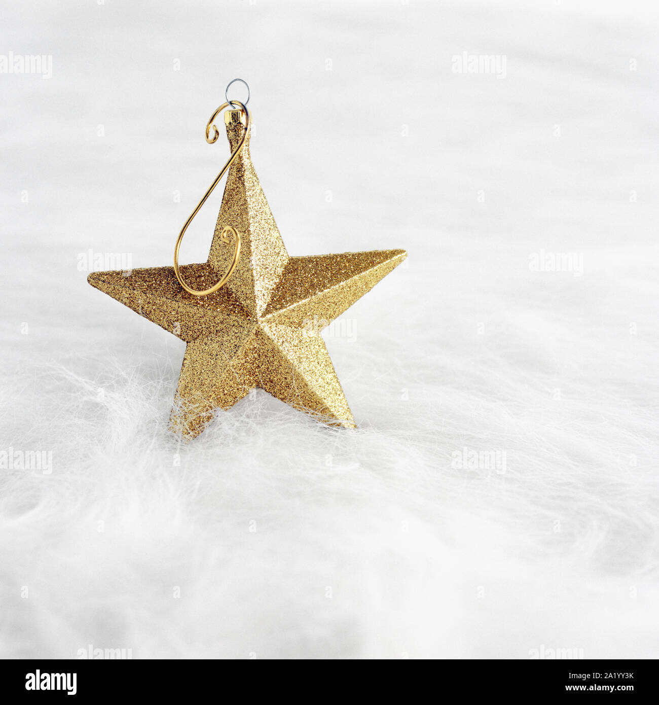 Close-up closeup of gold glitter star shaped Christmas ornament on white fur background. Elegant, fancy, shiny, bright holiday decorations. Stock Photo