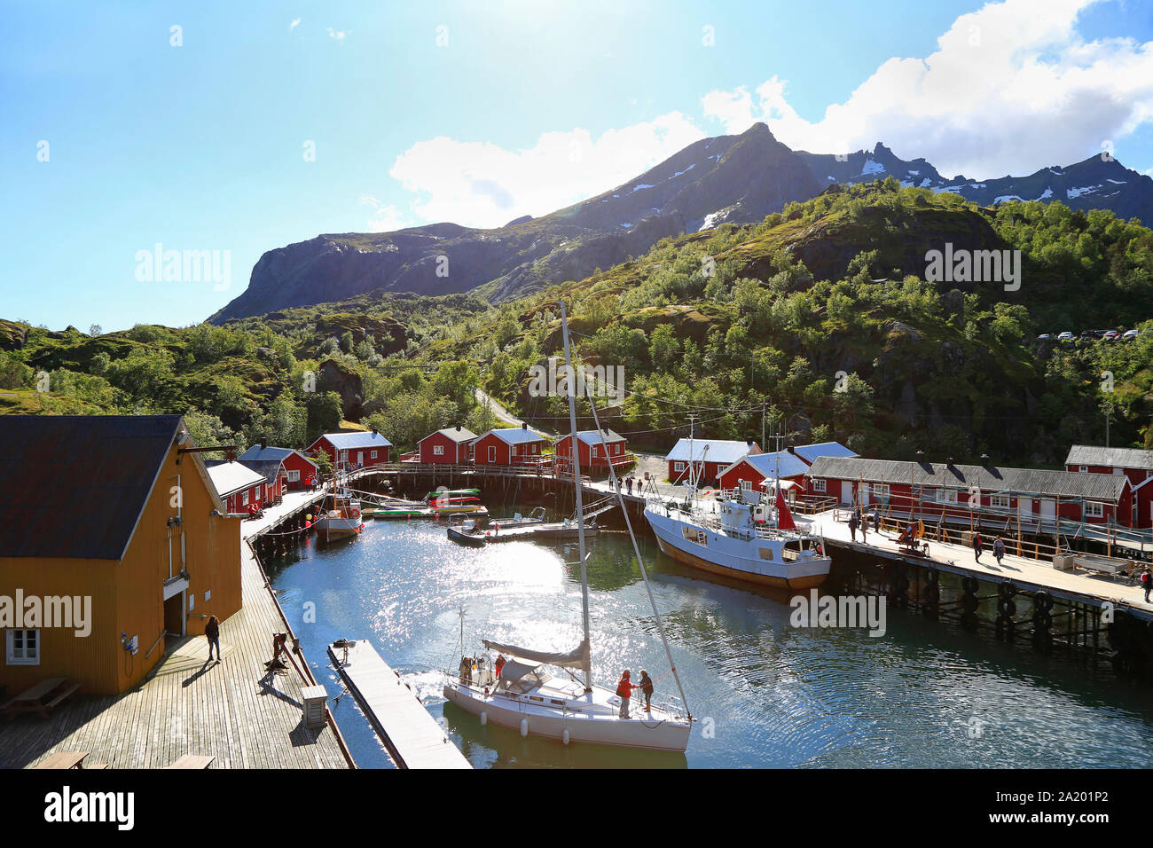 Nusfjord harbor with colorful red fishing houses and sailing boat in a sunny day, Lofoten Islands, Norway Stock Photo