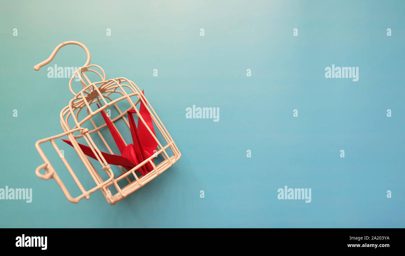 Top view of a red origami crane inside a small metal bird cage, with the cage door opened. Stock Photo