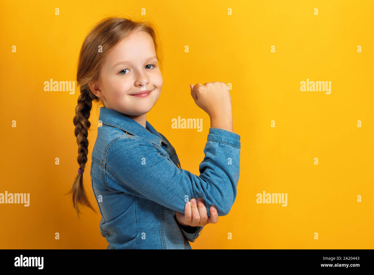 Closeup portrait of a little girl on a yellow background. Children's hand shows biceps. Girl power concept Stock Photo