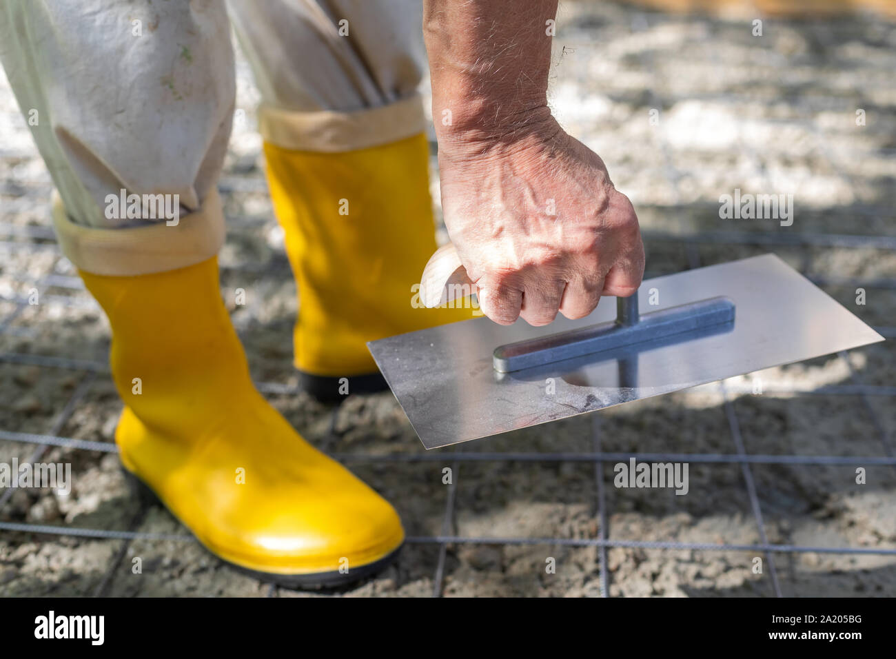 Construction worker in yellow rubber boots at the construction site, compacting the concrete
