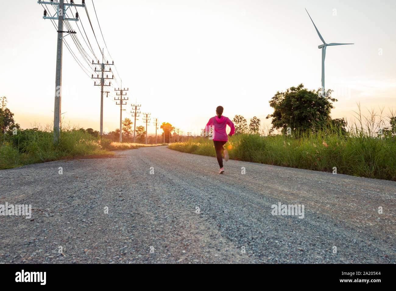The evening sunset, The area of the wind turbine generates clean energy electricity, A woman is jogging on the road. Stock Photo