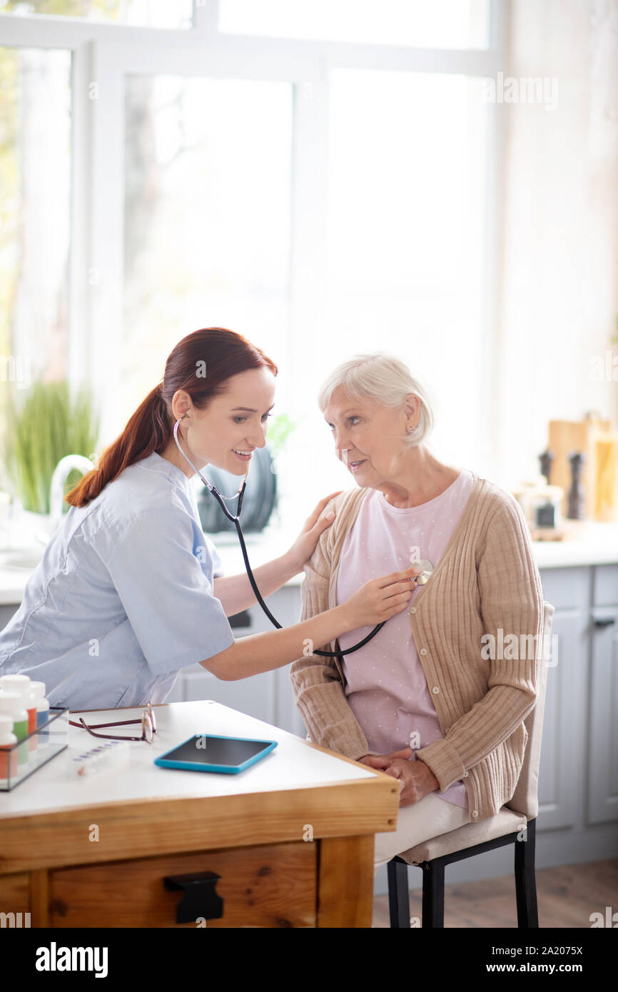 Medical attendant using stethoscope while visiting aged lady Stock Photo