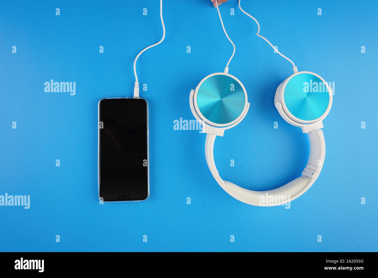 blue white color headphone placed next to handphone on a blue background Stock Photo