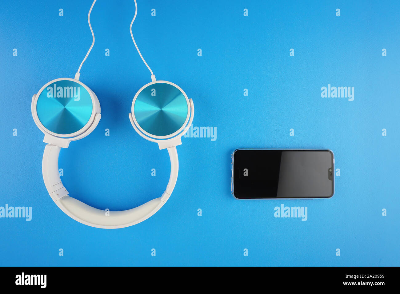 blue white color headphone placed next to handphone on a blue background Stock Photo