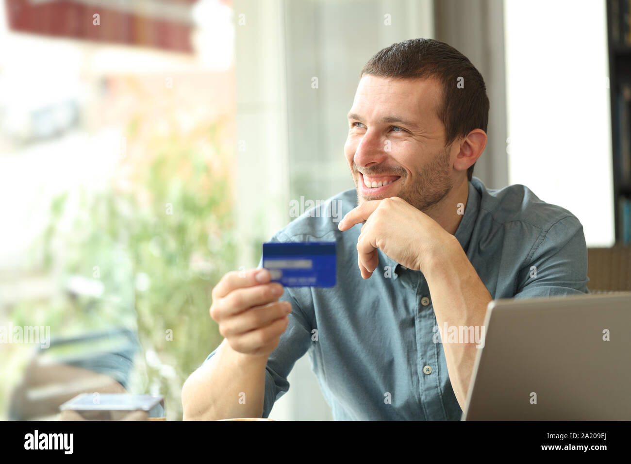 Happy adult buyer thinking holding a credit card looking at side