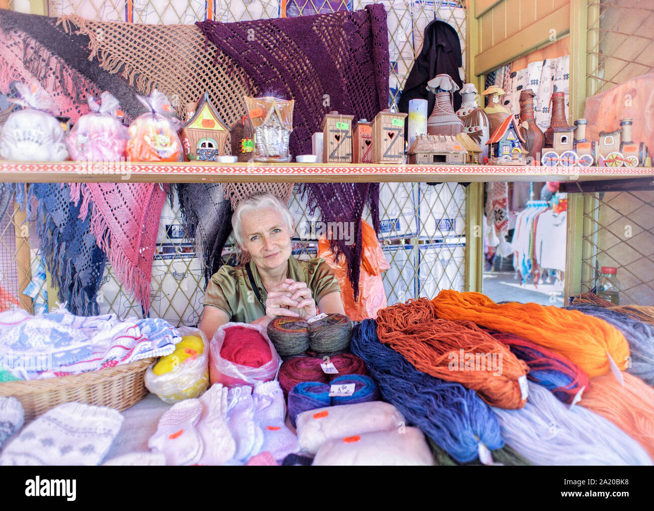 Environmental portrait of beautiful Estonian shopkeeper in the marketplace Tallinn, Estonia with souvenirs, wool, woolen goods and crafts for sale. Stock Photo