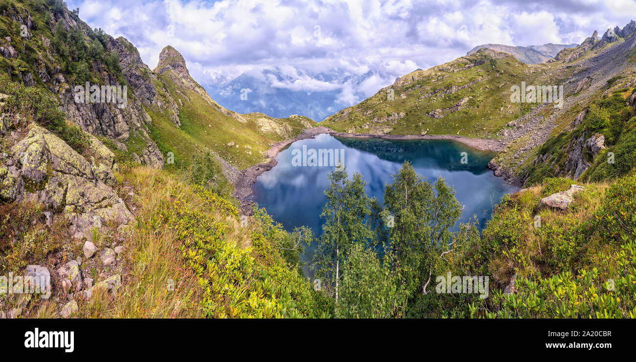 panorama landscape with clear lake in the mountains, huge rocks and Alpika and reflection of white clouds in Abkhazia in the Caucasus. Stock Photo