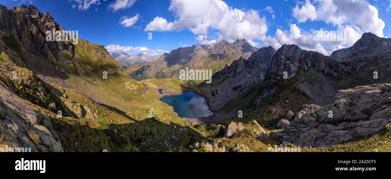 panorama landscape with clear lake in the mountains, huge rocks and Alpika and reflection of white clouds in Abkhazia in the Caucasus. Stock Photo