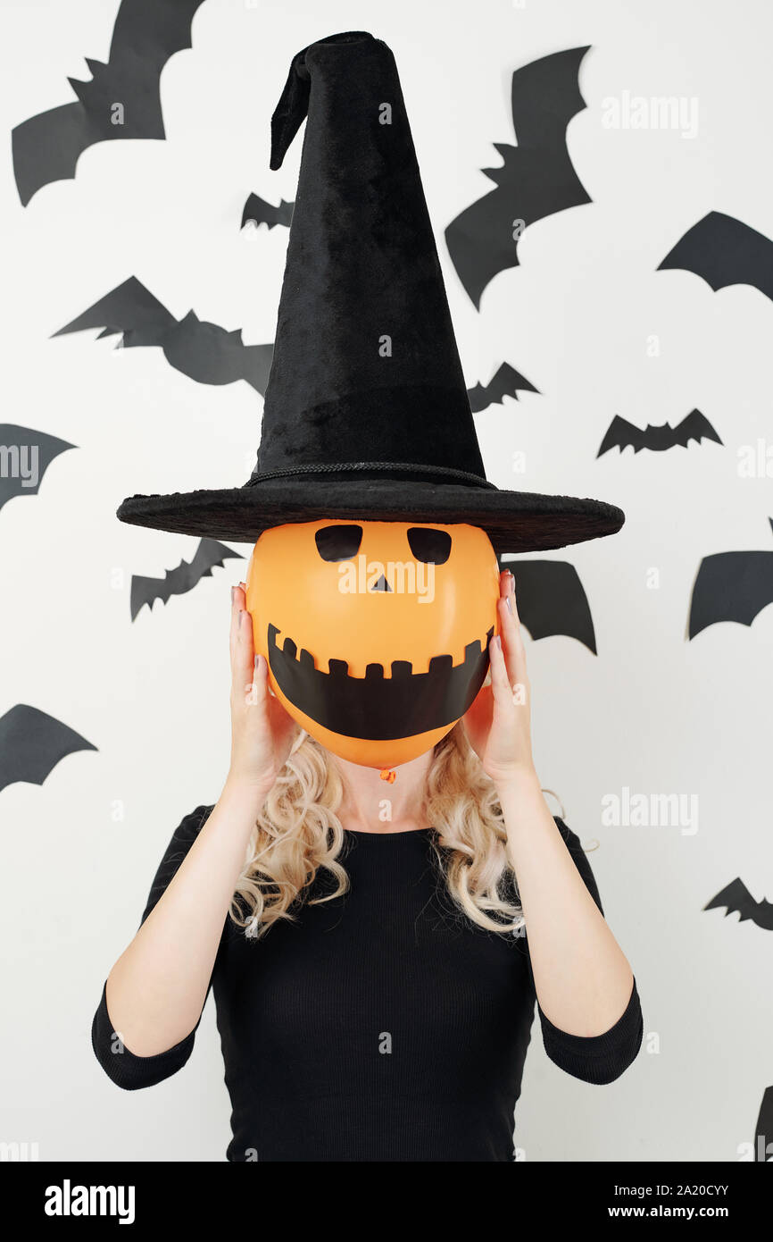 Young woman in conical hat holding orange balloon woth creepy smiling face in front of her head Stock Photo
