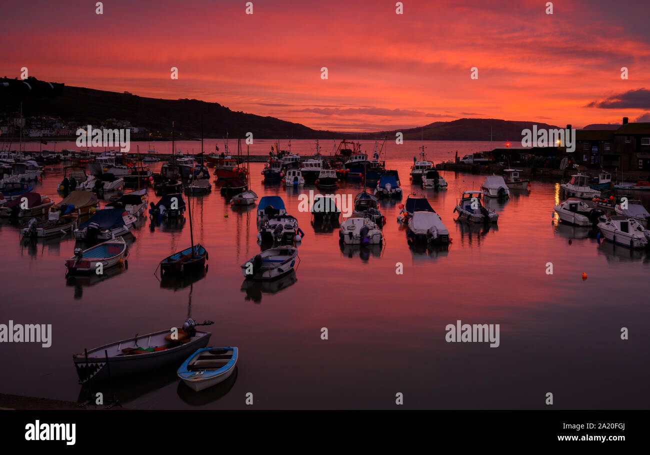 Lyme Regis, Dorset, UK. 30th September 2019. UK Weather: Red sky in the morning shepherd's warning.... The sky glows with vibrant red colour over boats moored at the Cobb Harbour at Lyme Regis at sunrise. Credit: Celia McMahon/Alamy Live News. Stock Photo