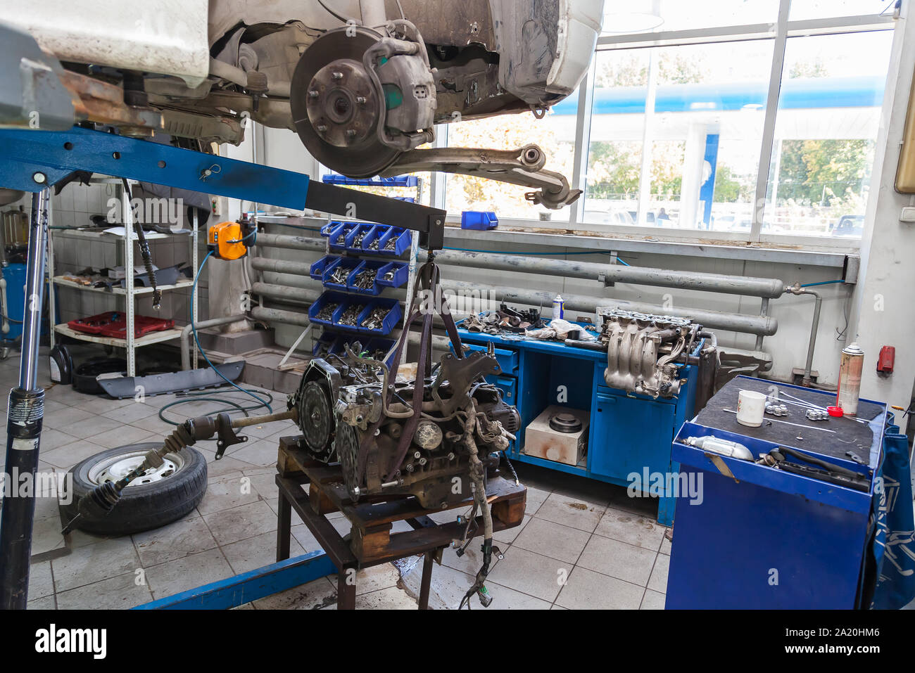 A white car raised on a lift for repair and under it a detached engine ...