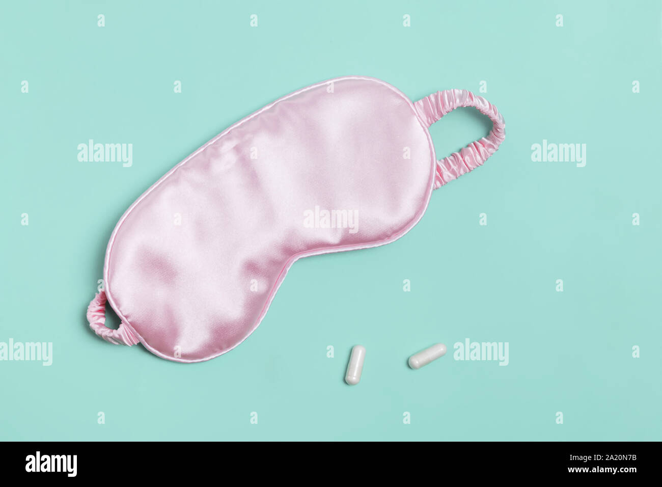 Sleeping mask and pills on pastel green background. Stock Photo