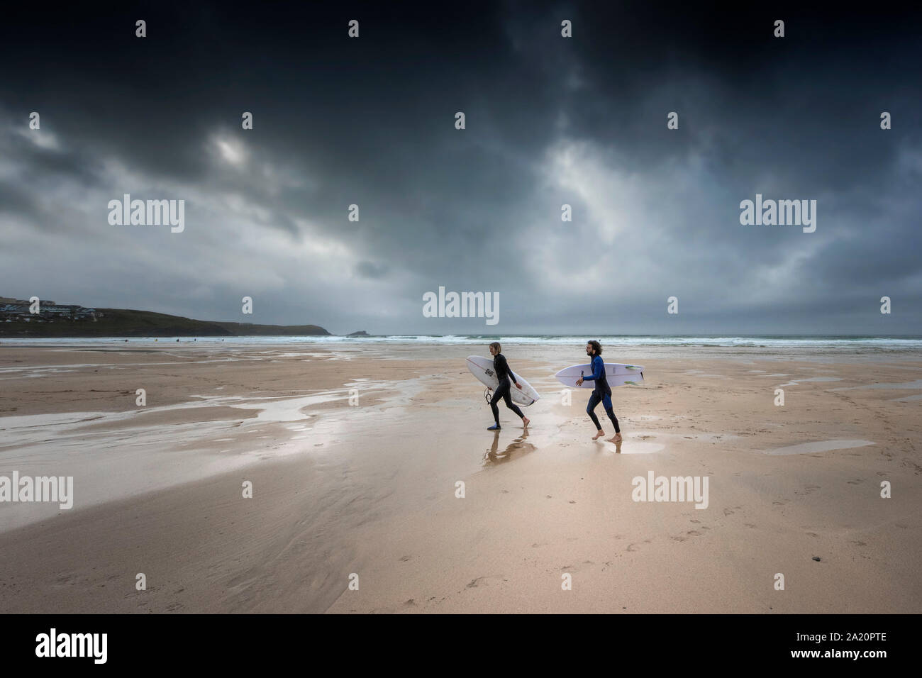 Surfers walking on Fistral Beach as dark gloomy storm clouds approach in Newquay in Cornwall. Stock Photo