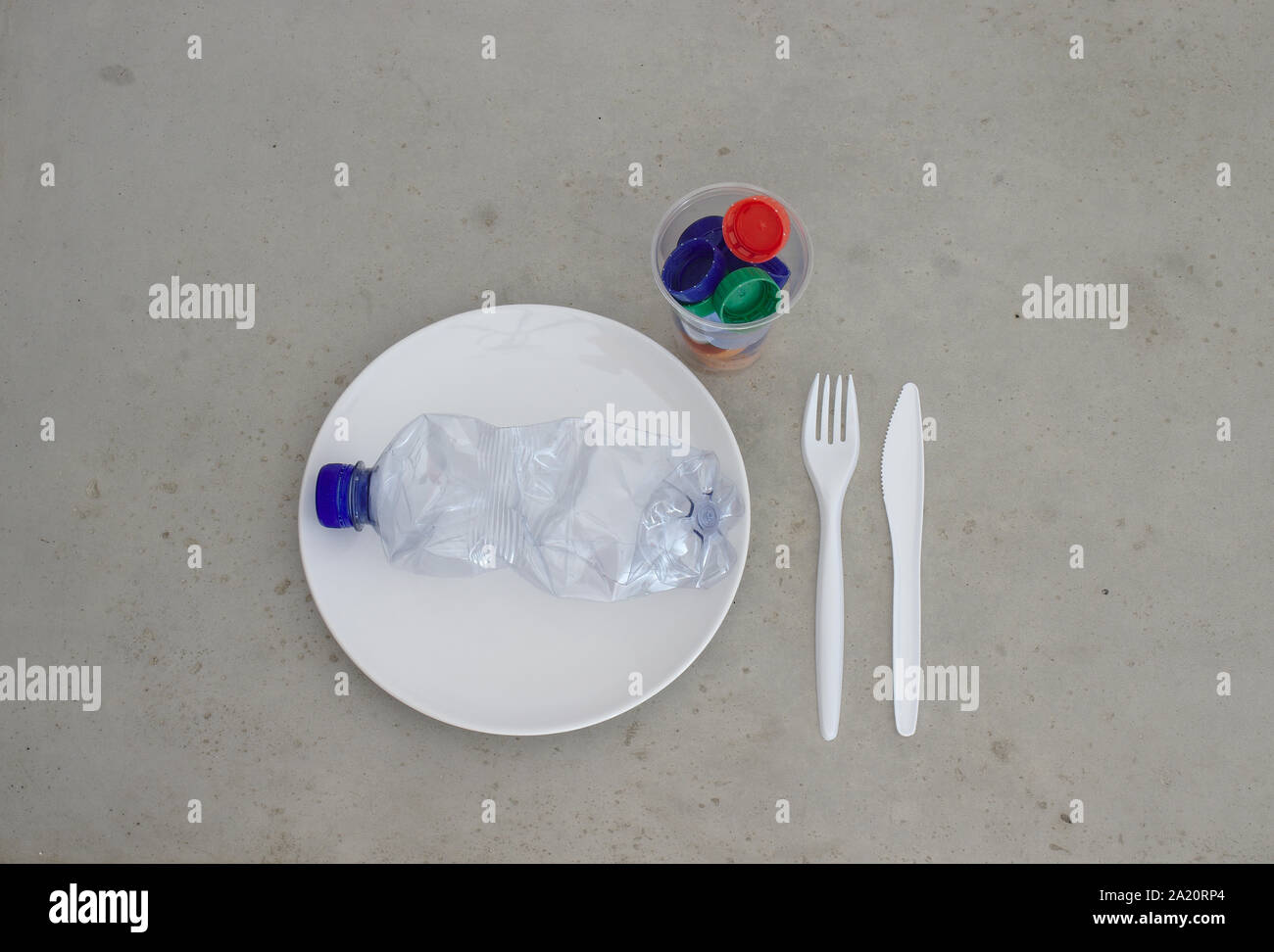 Pet plastic bottle on plate with cutlery and trash filled cup. Showing environment plastic pollution, recycling, zero waste and reusability concepts. Stock Photo