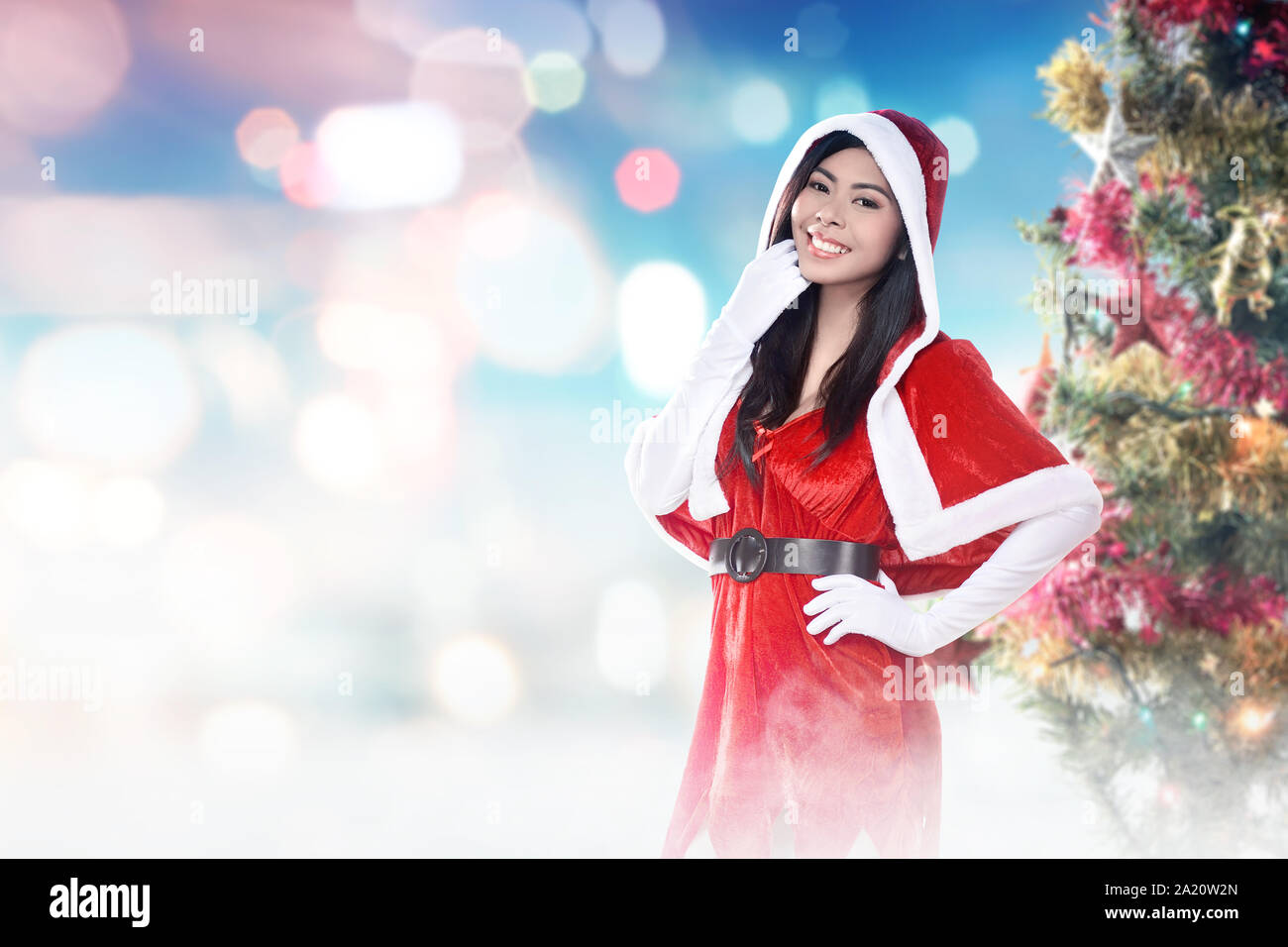 Asian woman in Santa costume standing with a decorated Christmas tree ...