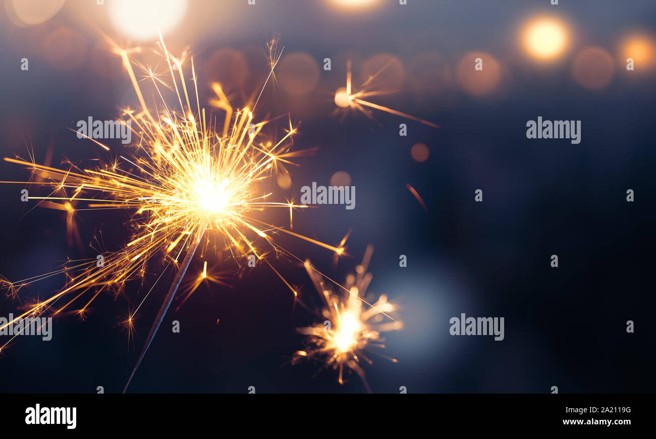 Glittering burning sparkler against blurred bokeh light background Stock Photo