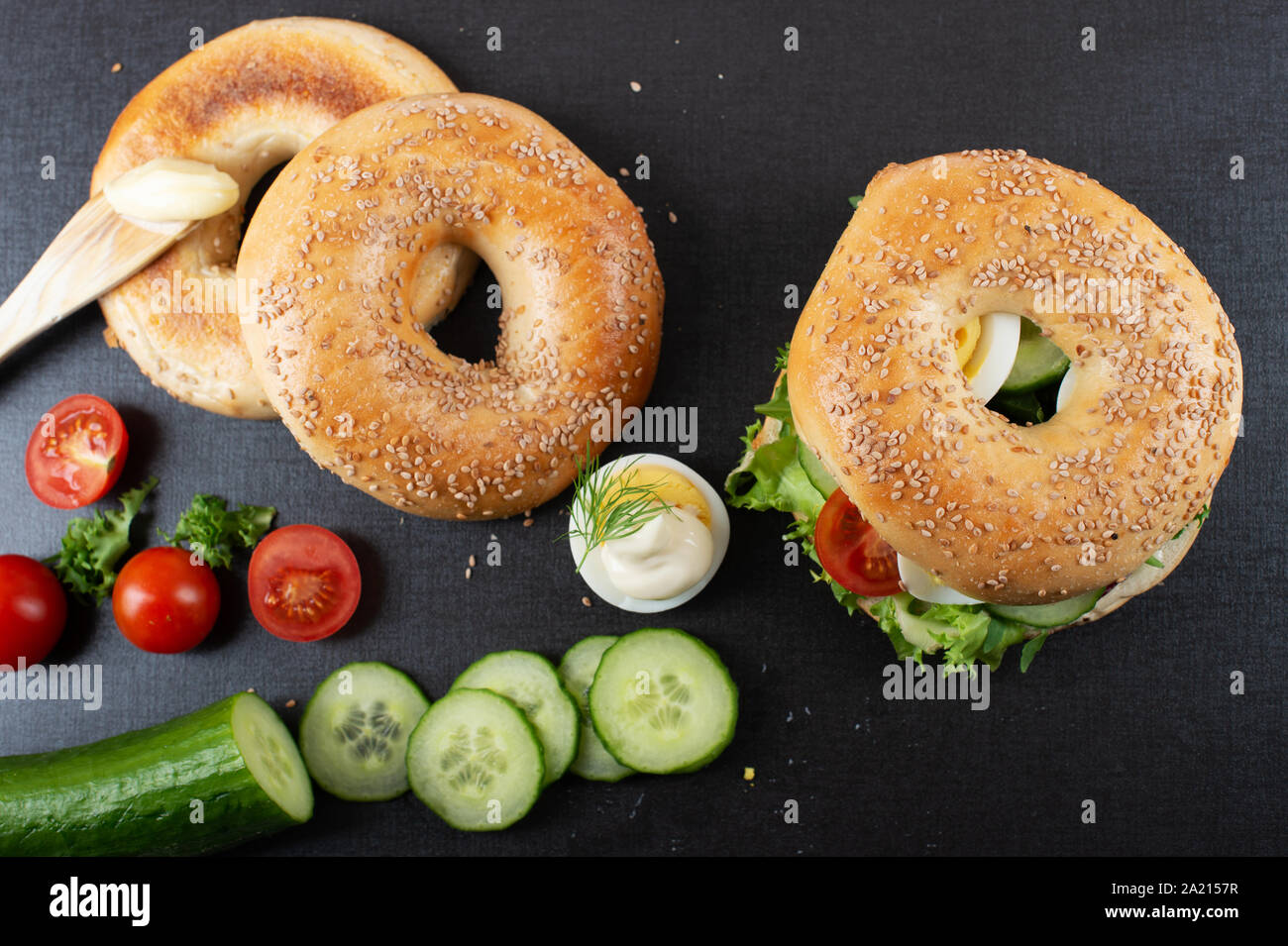 Fresh bagel with sesame seeds. Organic sliced eggs, tomato, lettuce, cucumber and tomato, mayonnaise. Stock Photo