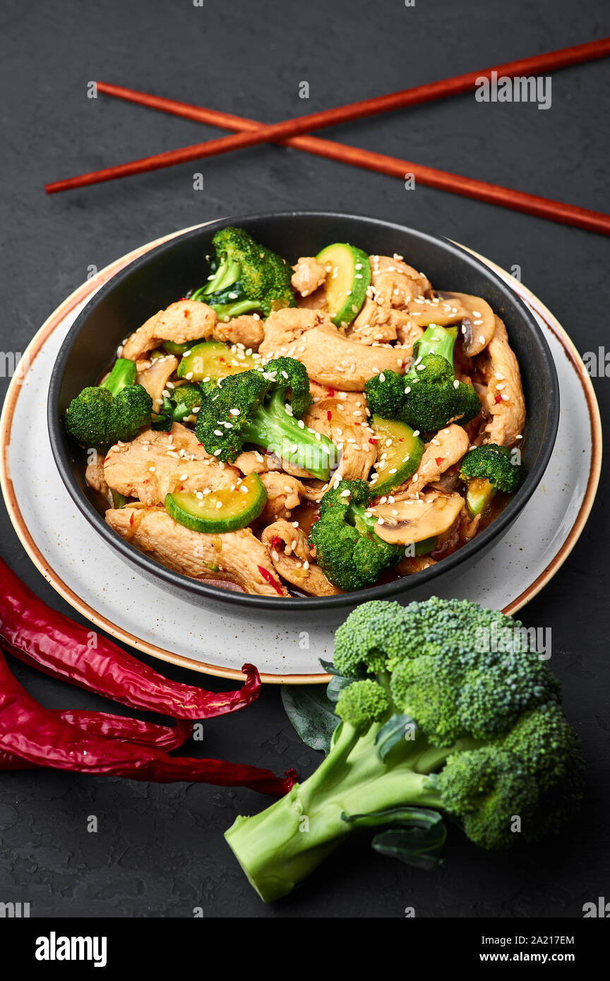 Hunan Chicken with ingredients in black bowl at dark slate background. Hunan Chicken is chinese or indo-chinese cuisine takeaway dish with broccoli, z Stock Photo