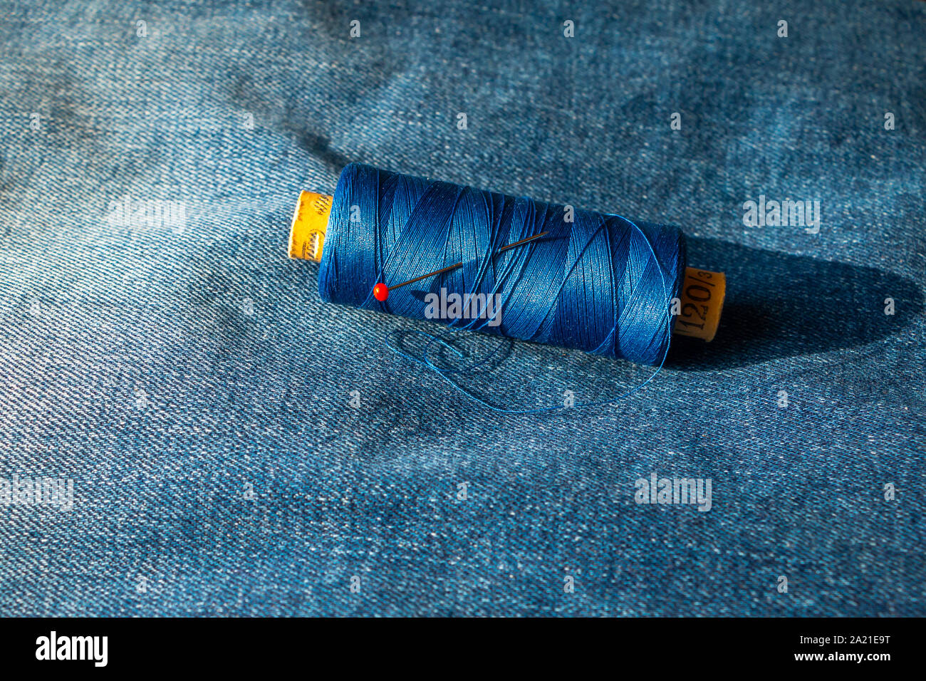 Spool of thread on a blue jeans with a round head pin put in the spool, picture taken in the Netherlands Stock Photo