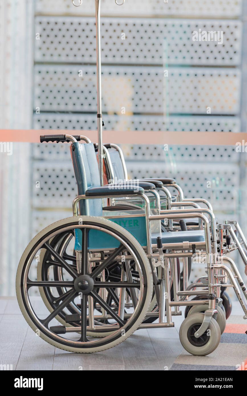 From side on a set of wheelchairs sit empty, waiting to be used in a bright sunny room near a window Stock Photo