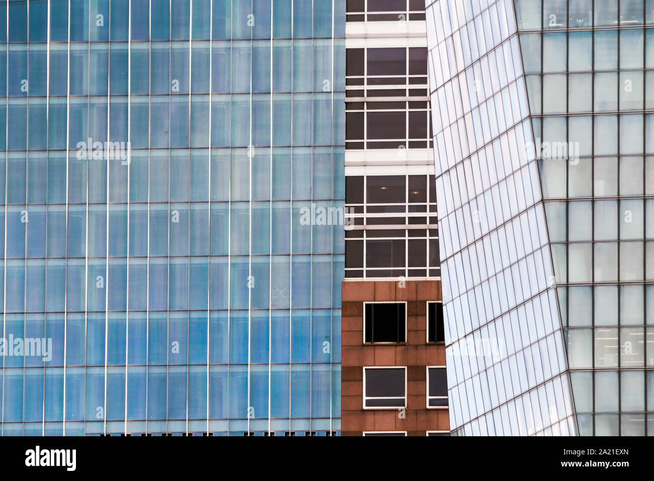 Close up of building facades showing contrast patterns as a different building reveals its face between a curtain of glass facades. Stock Photo