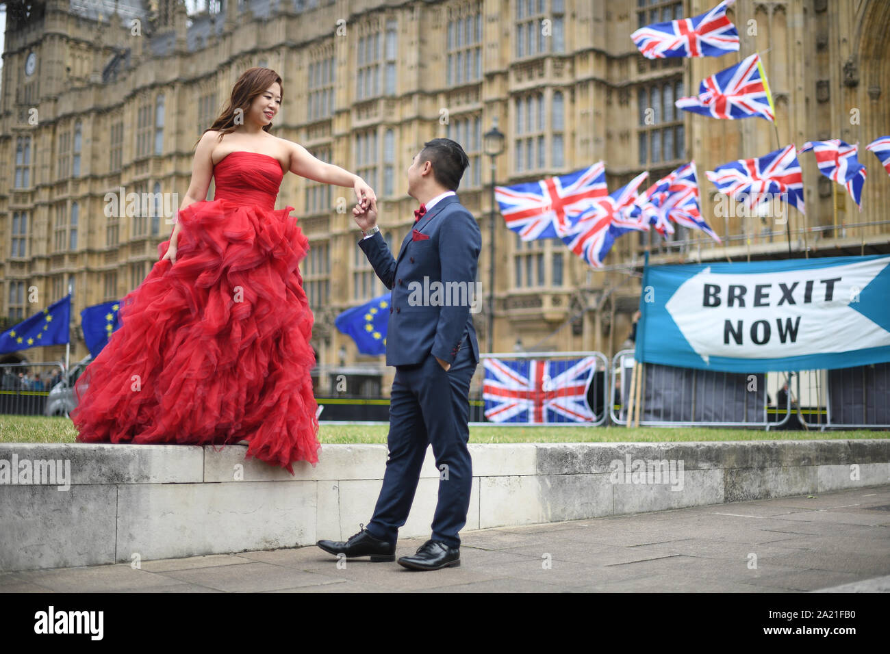 Two tourists posing for pictures in front of Union and EU flags outside the Palace of Westminster, London. Stock Photo