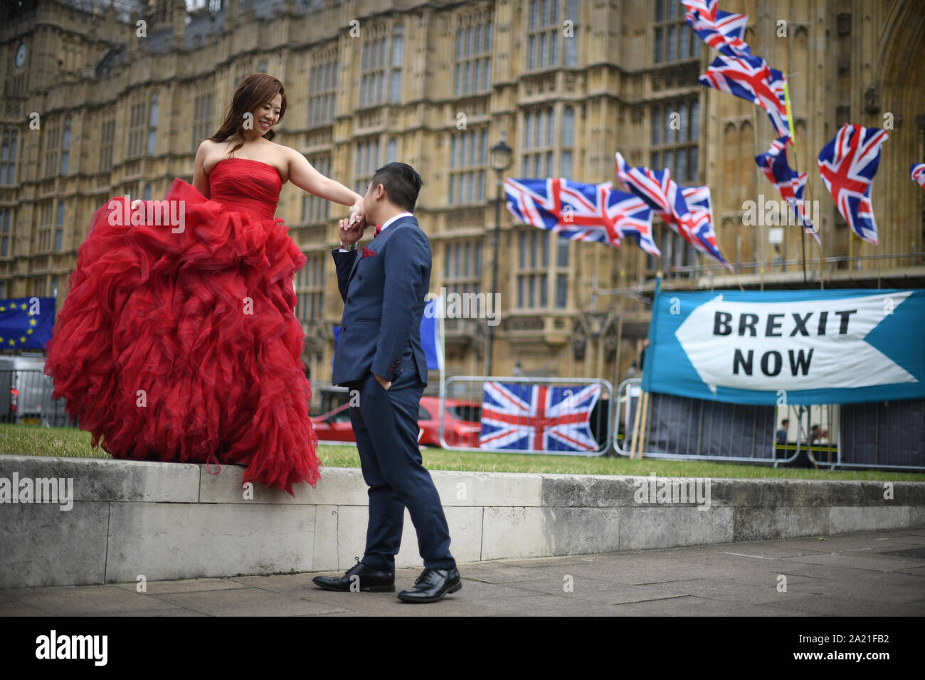 Two tourists posing for pictures in front of Union and EU flags outside the Palace of Westminster, London. Stock Photo