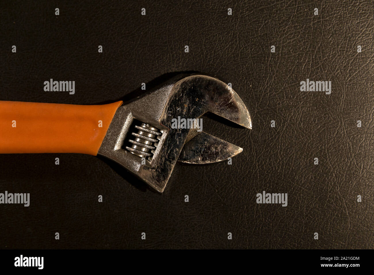 Top view close up of the head of an adjustable wrench with plastic orange handle, lying on leather surface. Stock Photo