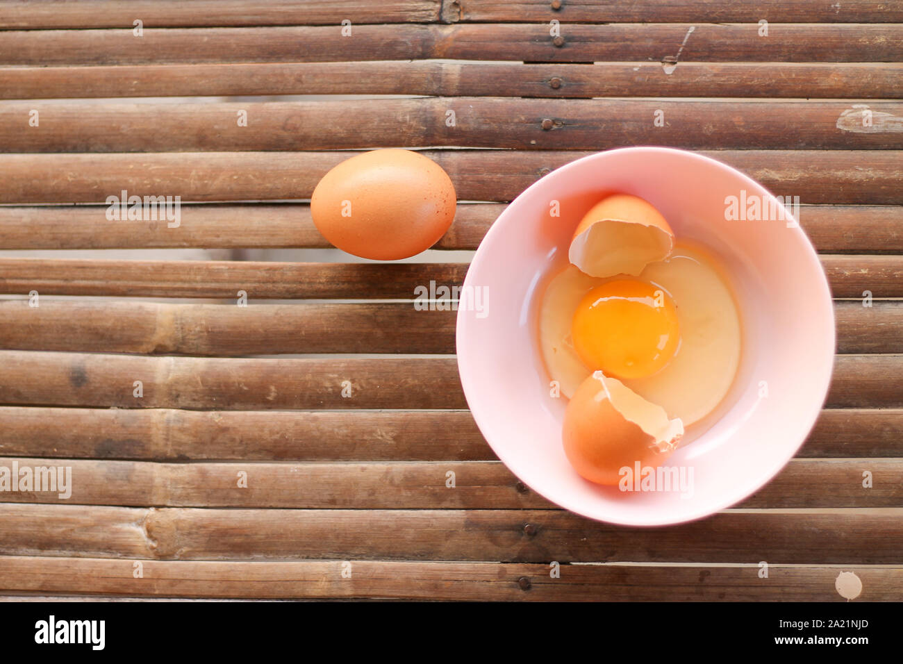 shell with egg and open Eggs in a pink bowl on Bamboo battens. Top view closeup Stock Photo