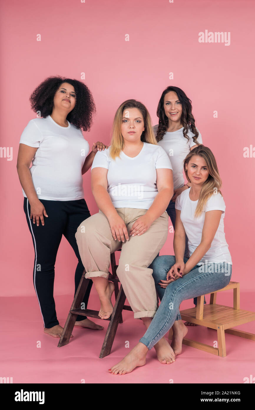a group of young girls in white t shirts and jeans pose for the camera on a delicate pink background casual clothing style 2A21NKG
