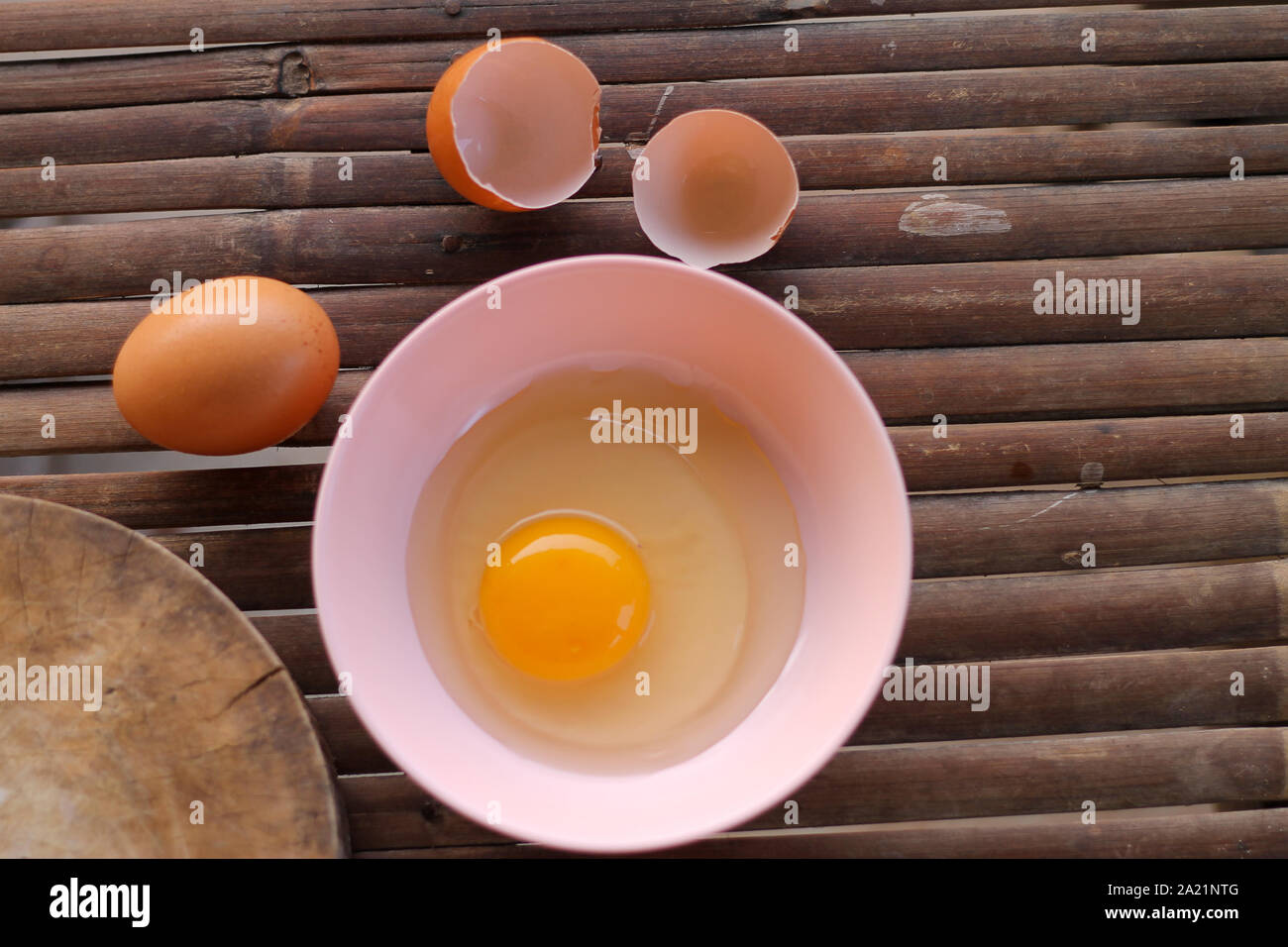 shell with egg and open Eggs in a pink bowl Placed near to the butcher on Bamboo battens.Top view closeup. Stock Photo