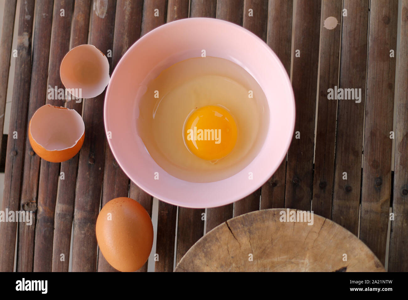 shell with egg and open Eggs in a pink bowl Placed near to the butcher on Bamboo battens.Top view closeup. Stock Photo
