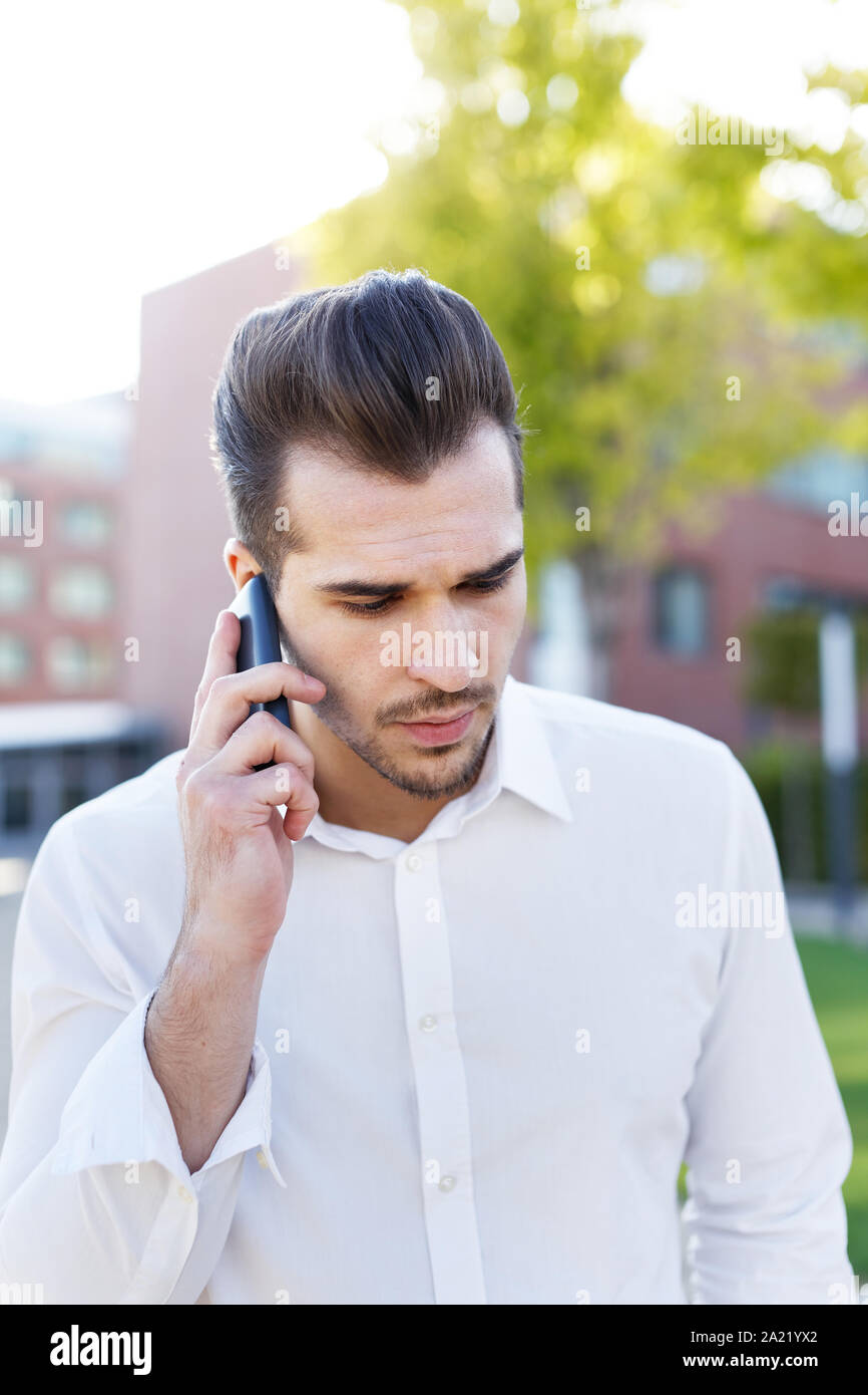 Young caucasian businessman calling in park looking down Stock Photo