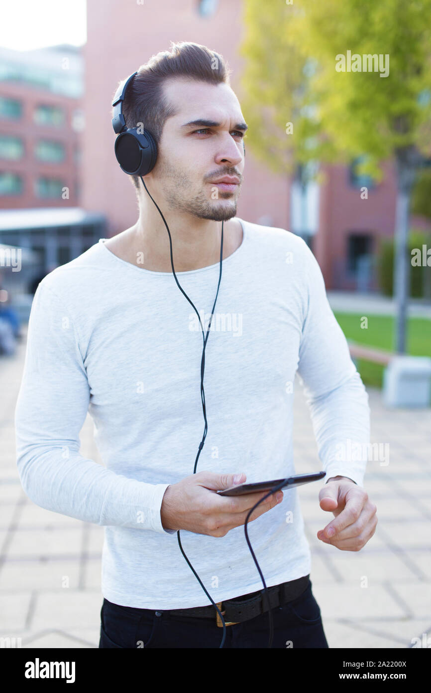 Young man in casual wear listening music in autumn park by headphones Stock Photo