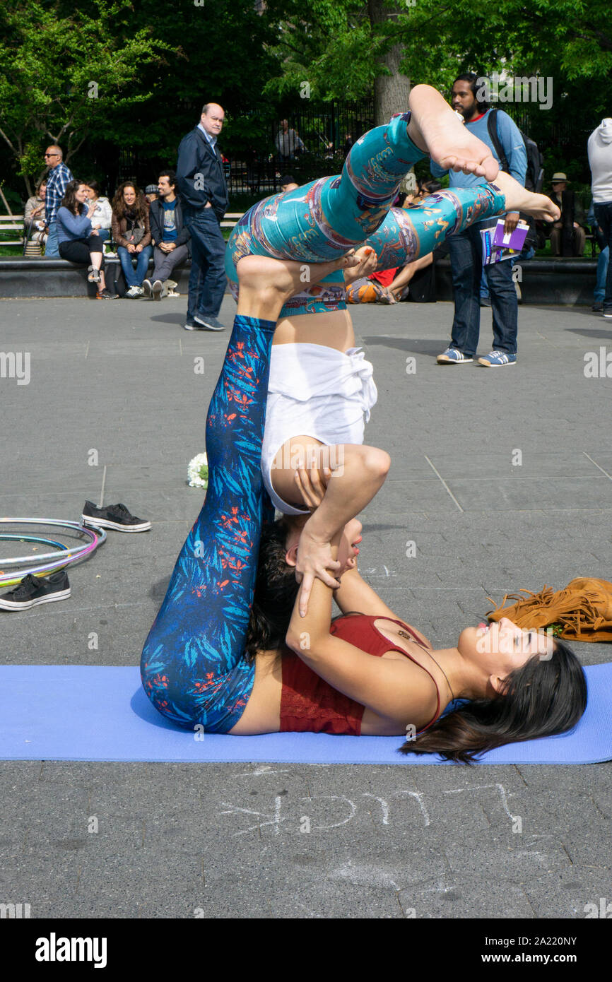 Two young ladies do acroyoga exercises in front of a crowd near the fountain in Washington Square Park, New York City. Stock Photo