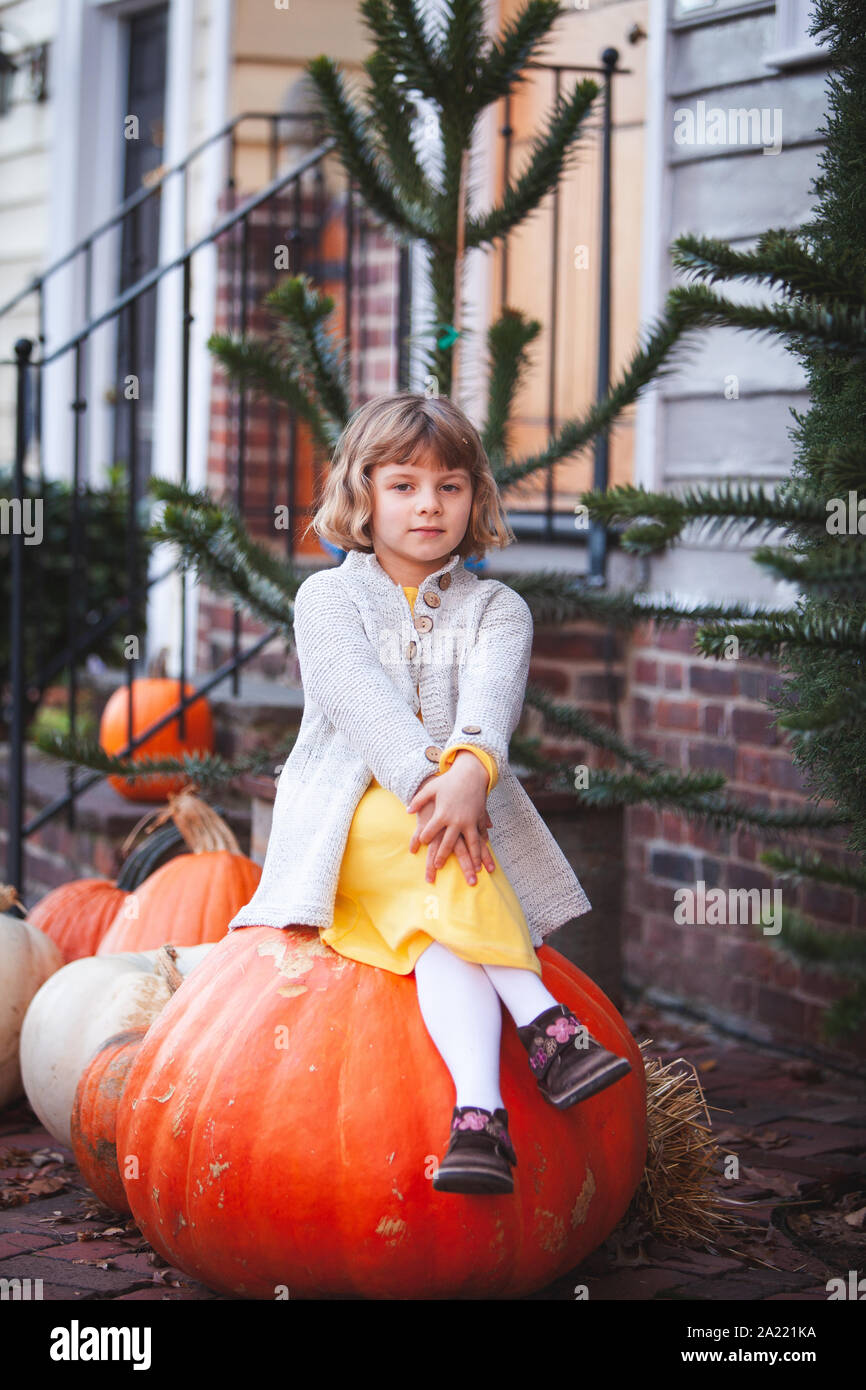 Little girl is sitting on the big orange pumpkin in Old Town Alexandria, Virginia Stock Photo