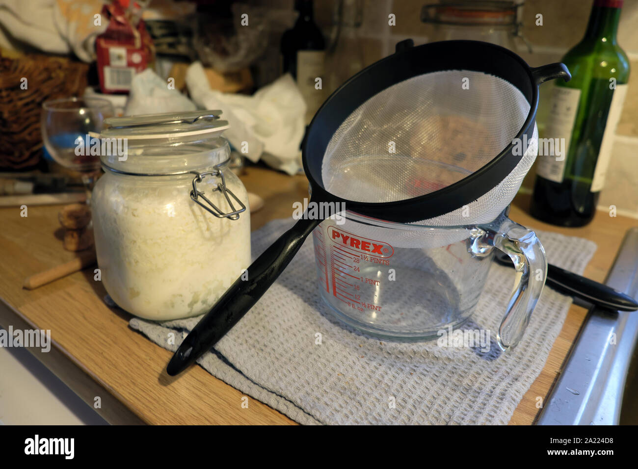 Utensils for making kefir a homemade organic probiotic made by fermentation with whole milk in a kilner jar in a kitchen at home Wales UK KATHY DEWITT Stock Photo
