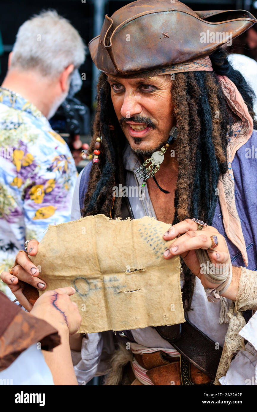 Pirate Day in Hastings, UK. Close up of a young man dressed up as Captain Jack Sparrow holding out a cloth treasure map with symbols. No eye-contact. Stock Photo