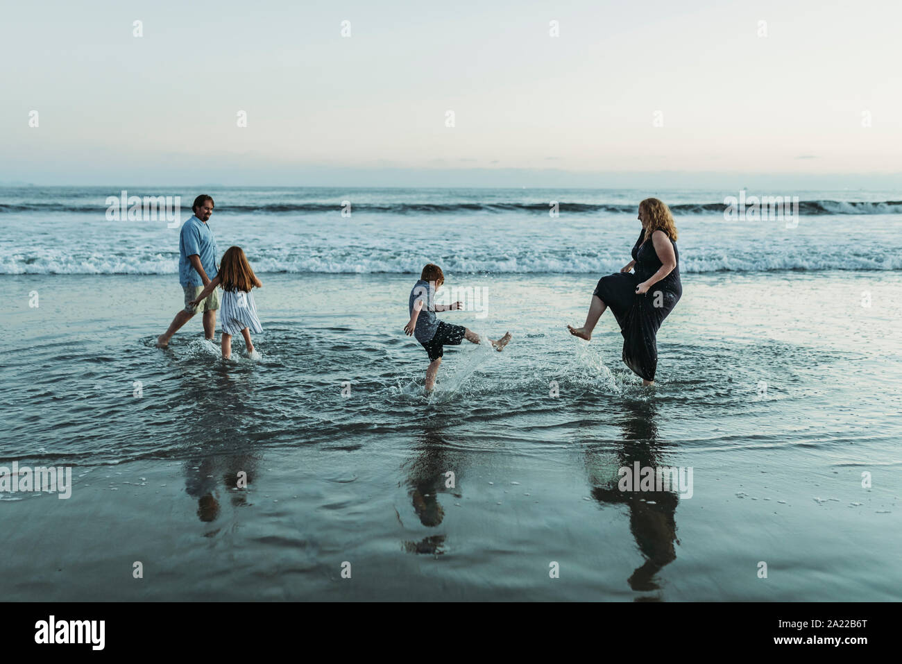 Family of four playing and splashing each other in ocean at dusk Stock Photo