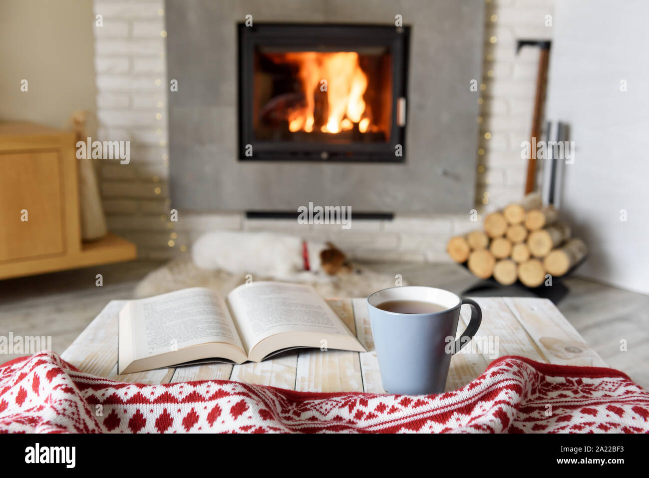 Hygge concept with open book and cup of tea near burning fireplace Stock Photo
