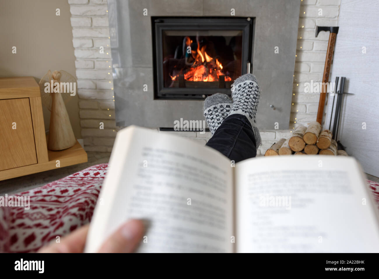 Hygge concept with open book in man hands near burning fireplace Stock Photo