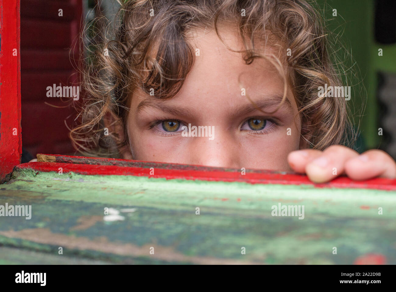 Girl with green eyes, leaning on the window of a colorful wooden house Stock Photo