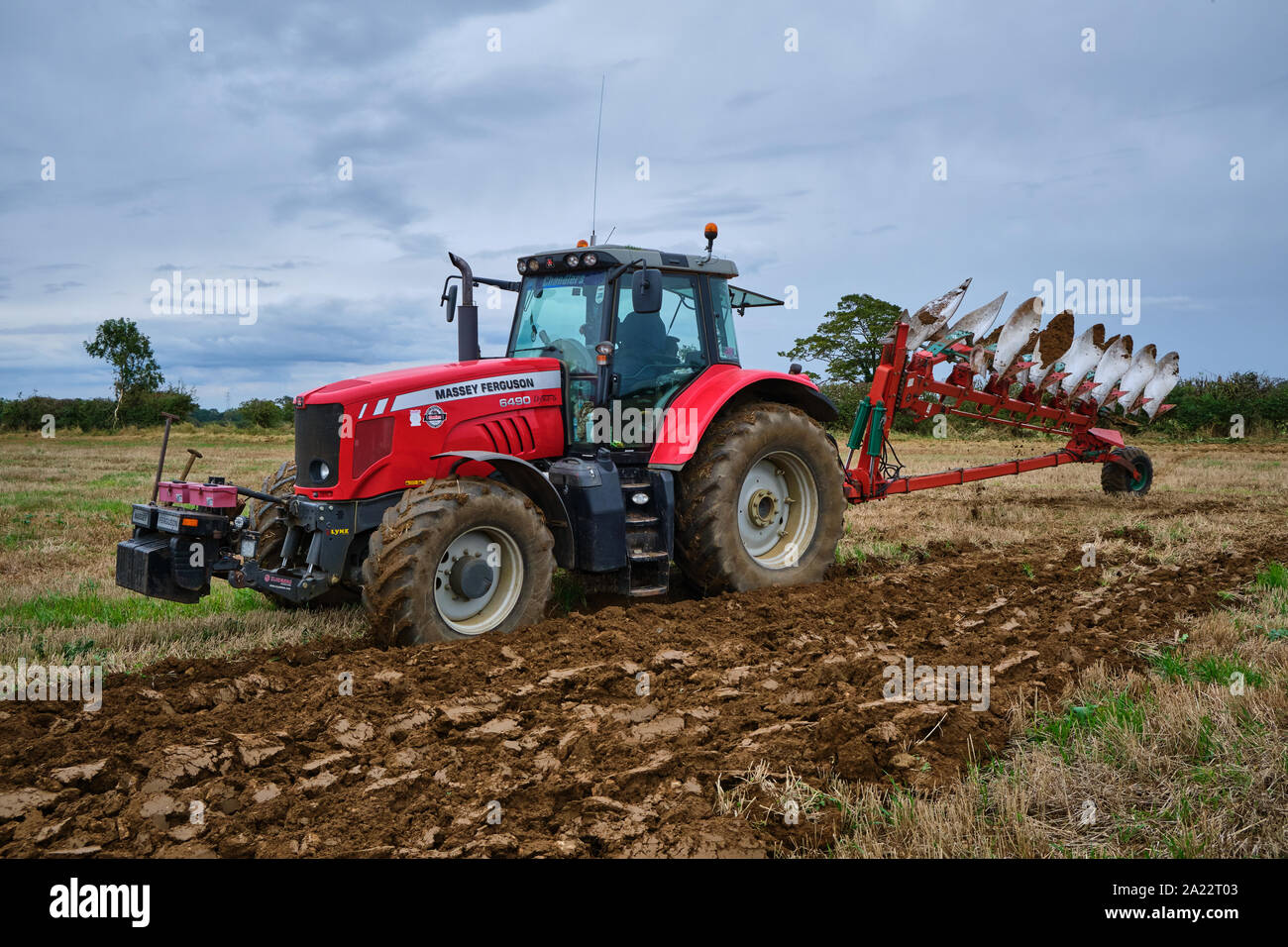 Red Massey Ferguson agricultural 6490  tractor turning over a 6 furrow reversible Kverneland PB100-8 semi-mounted plough at the field headland Stock Photo