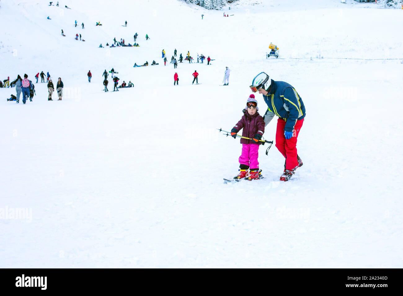Bansko, Bulgaria - December, 12, 2015: The small child learning to ski and man on the slope in Bansko, Bulgaria Stock Photo
