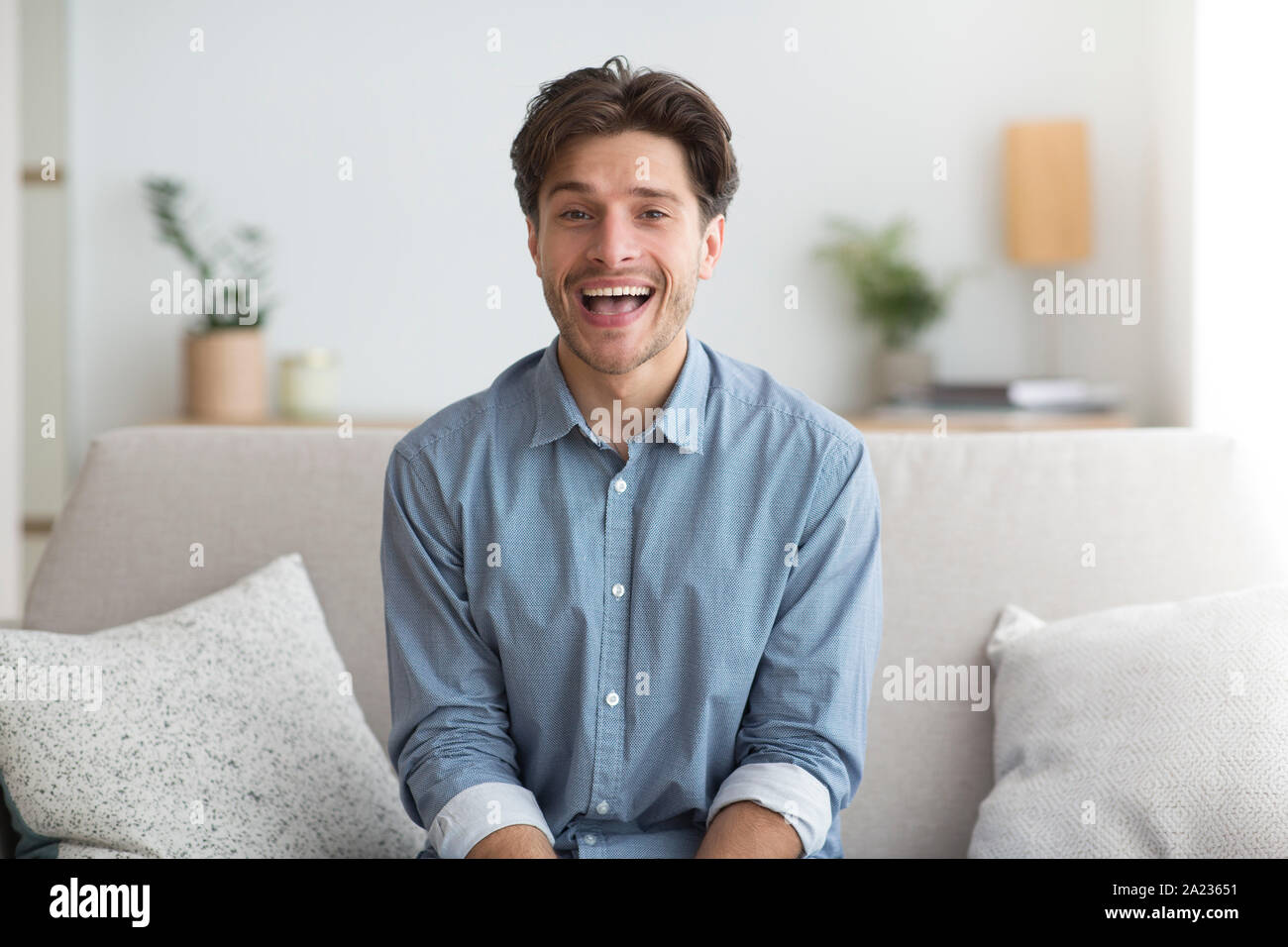 Happy Guy Smiling At Camera Sitting On Sofa At Home. Good Mood Concept Stock Photo