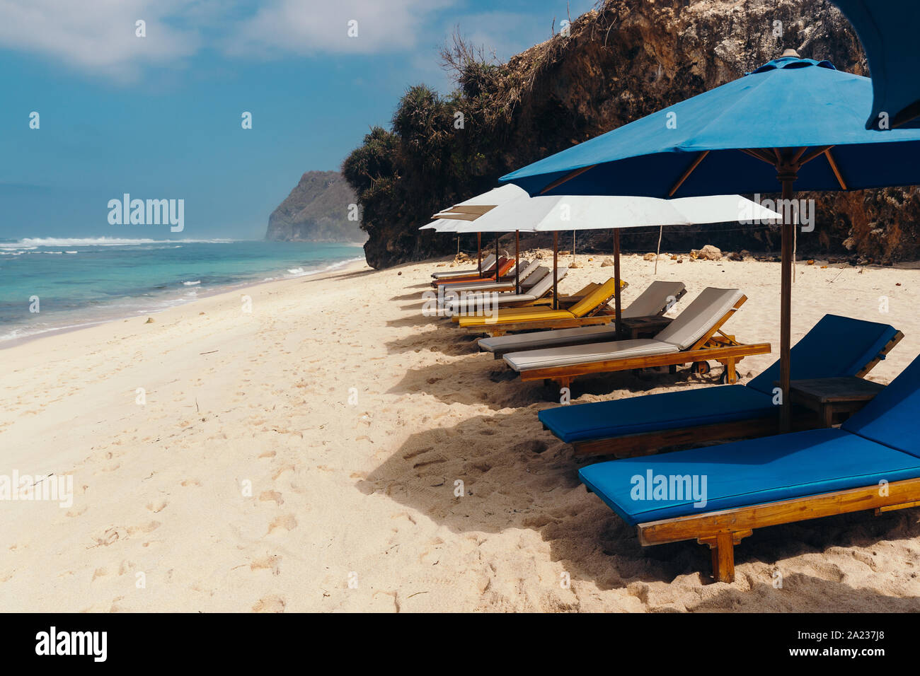 Wooden deck chairs with umbrellas along the coastline. Melasti Beach in the Indian Ocean. Indonesia, Bali. Stock Photo