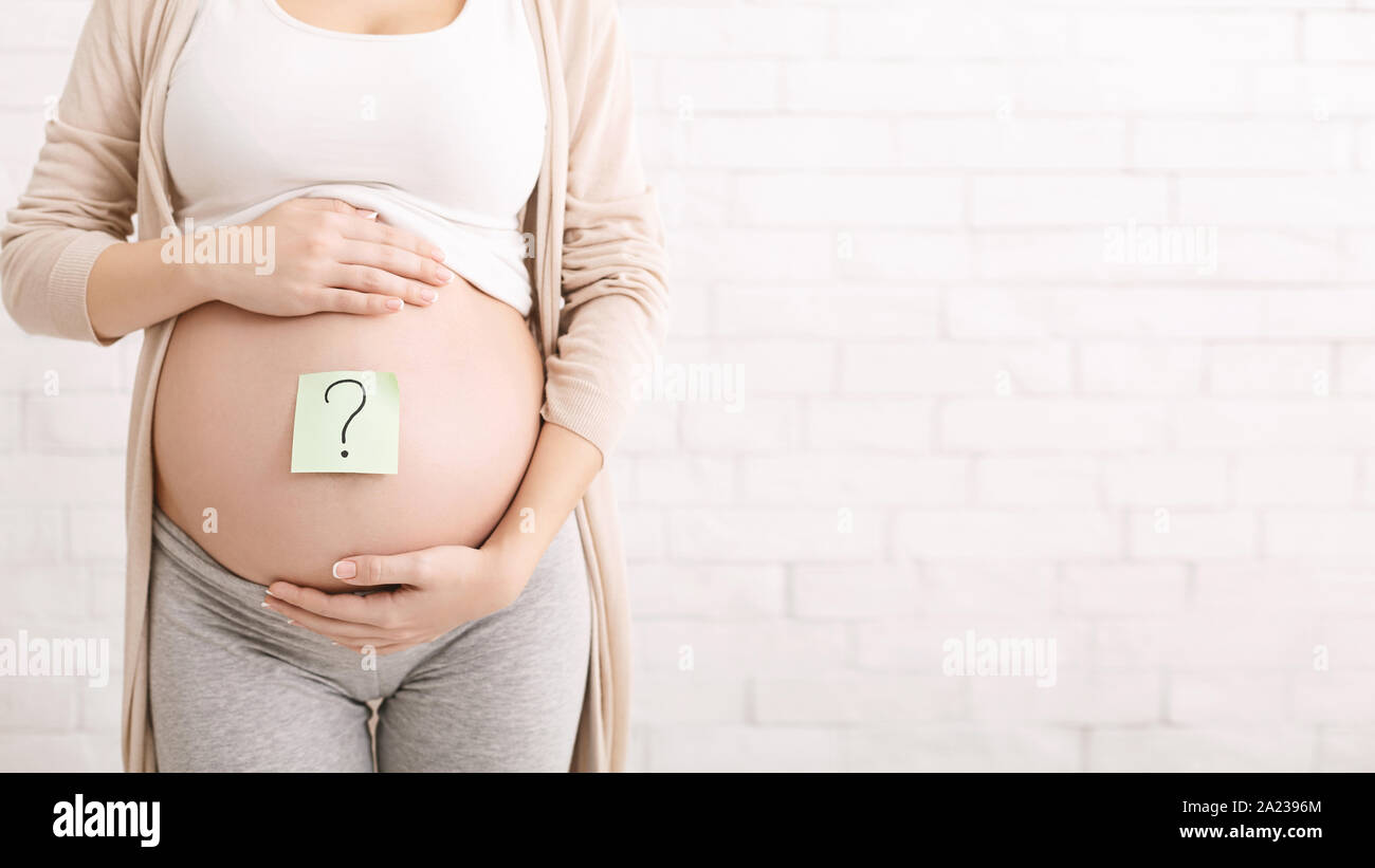 Choosing baby name. Pregnant woman embracing her belly with question mark on it, panorama with free space Stock Photo